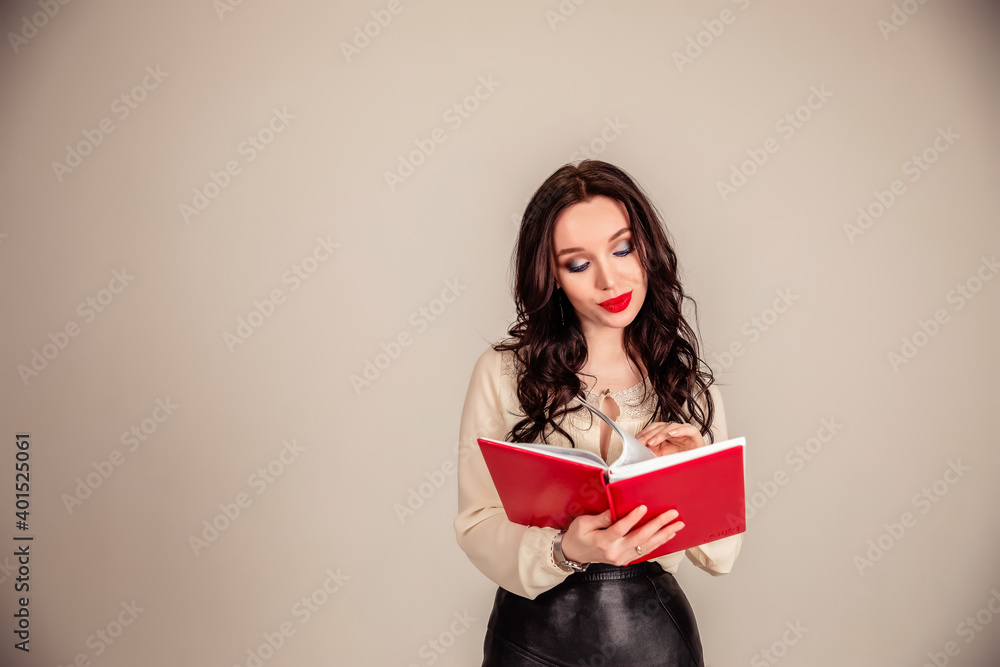 a beautiful young girl with red lips holds a red notebook in her hands. student on isolated gray background. education. Copy space a beautiful young girl with red lips holds a red notebook in her hands. student on isolated gray background. education. Copy space