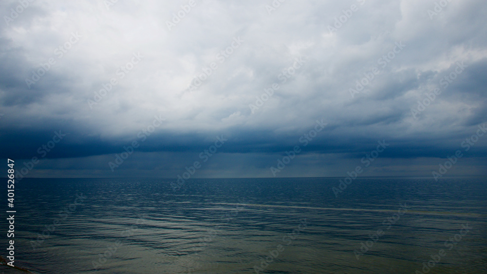Moody dramatic dark contrasting clouds over calm sea. Storm approaching. Moody dramatic dark contrasting clouds over calm sea. Storm approaching.