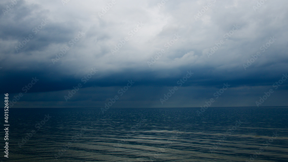 Moody dramatic dark contrasting clouds over calm sea. Storm approaching. Moody dramatic dark contrasting clouds over calm sea. Storm approaching.