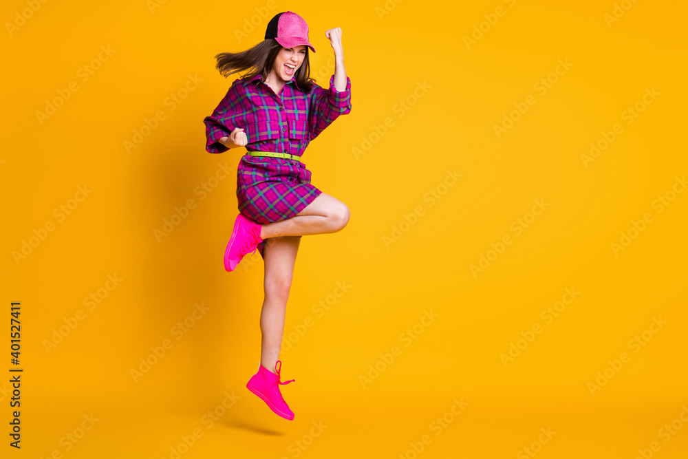 Full size portrait of attractive lady jumping won fist hooray wear plaid cap isolated on yellow color background Full size portrait of attractive lady jumping won fist hooray wear plaid cap isolated on yellow color background
