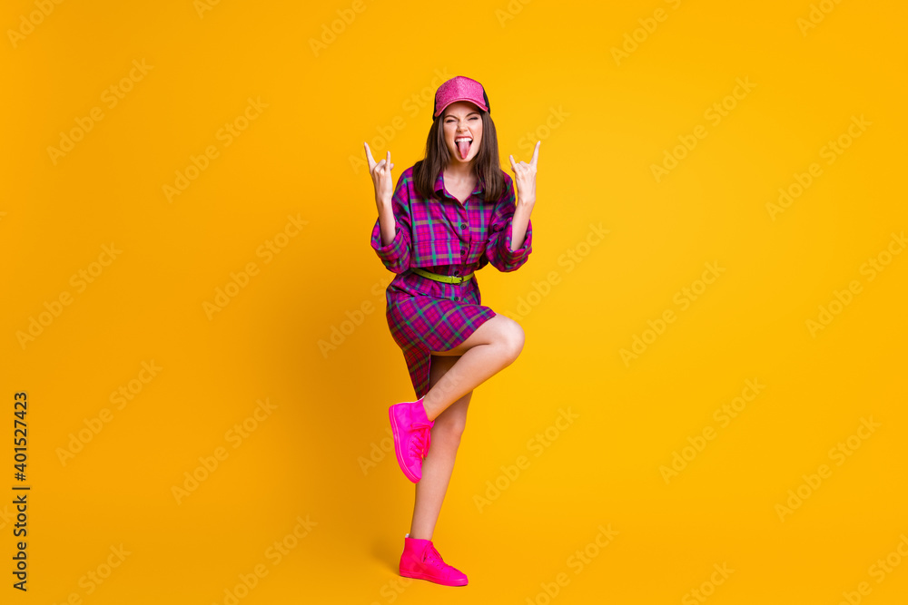 Full body portrait of childish girl tongue out show heavy metal sign stylish cap isolated on yellow color background Full body portrait of childish girl tongue out show heavy metal sign stylish cap isolated on yellow color background