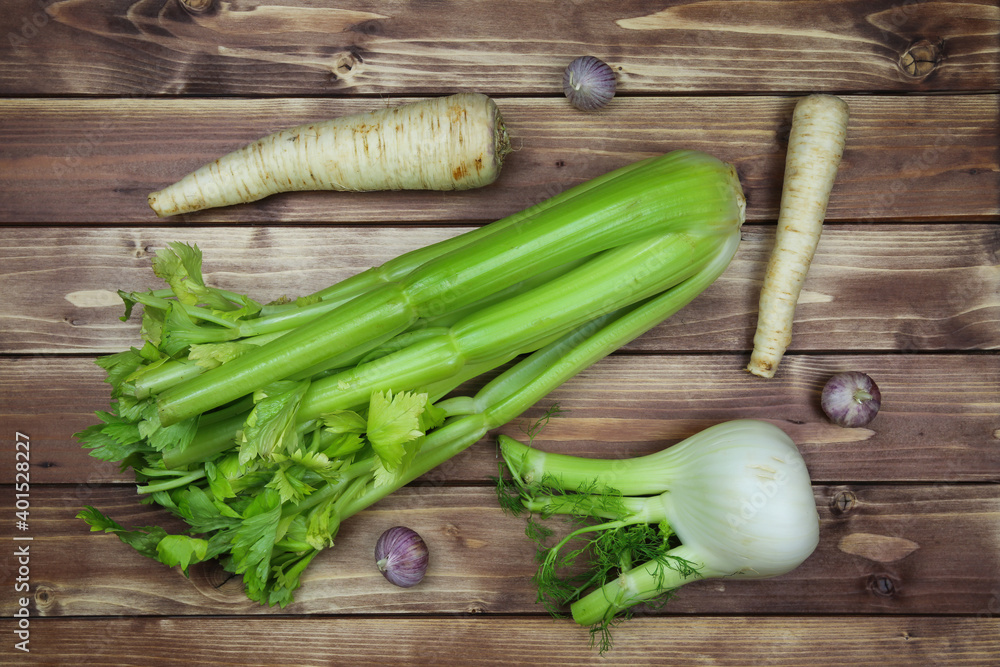 Top down view on raw uncooked isolated celery stalk, garlic and fennel bulbs, parsley roots. Brown natural rustic wooden background. Healthy ingredients for winter soup. Top down view on raw uncooked isolated celery stalk, garlic and fennel bulbs, parsley roots. Brown natural rustic wooden background. Healthy ingredients for winter soup.