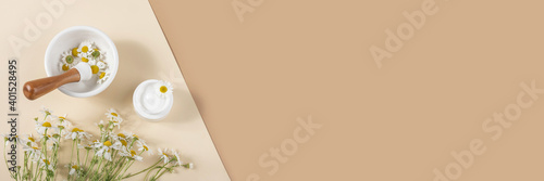 White cosmetic jar of cream, bouquet of chamomile flowers and mortar bowl with pestle on beige, brown background. Concept natural herbal organic cosmetic, homeopathic cosmetology. Banner photo