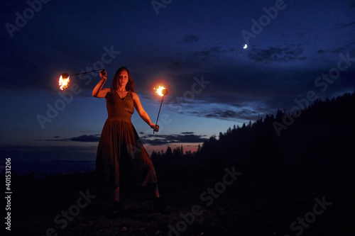 Fire show by woman in dress in night Carphatian mountains. Beautiful landscape