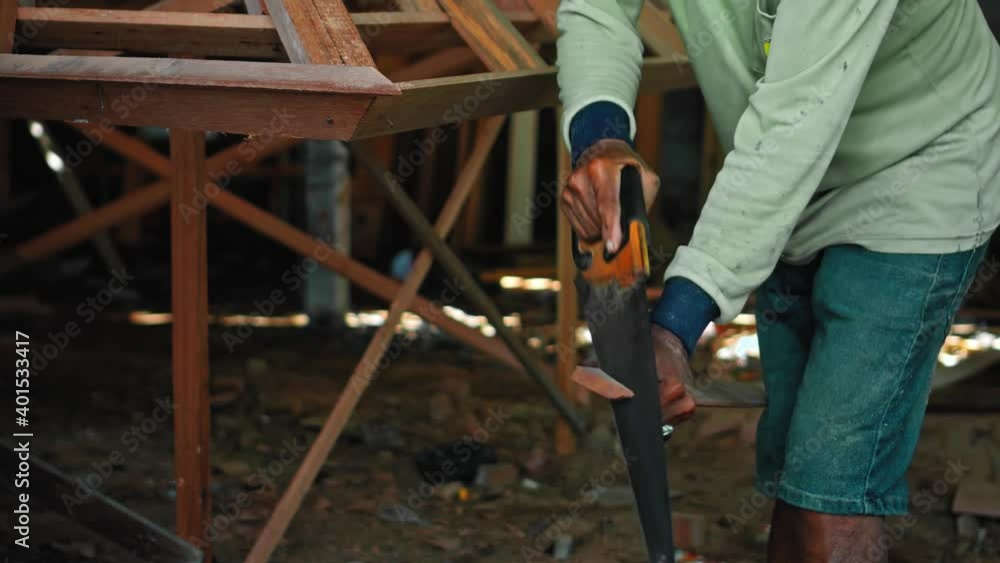 Old master with wrinkled hands saws a wooden board with a hand saw on wood in the workshop Old master with wrinkled hands saws a wooden board with a hand saw on wood in the workshop