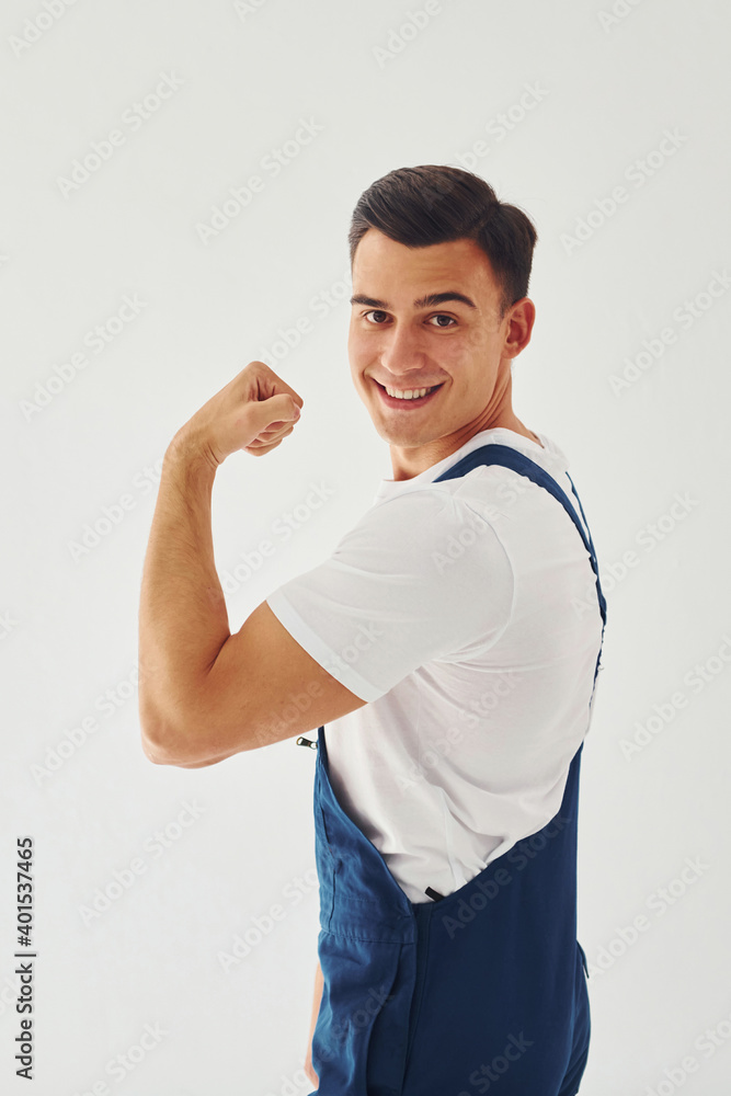 Shows biceps. Ready to work. Male worker in blue uniform standing inside of studio against white background Shows biceps. Ready to work. Male worker in blue uniform standing inside of studio against white background