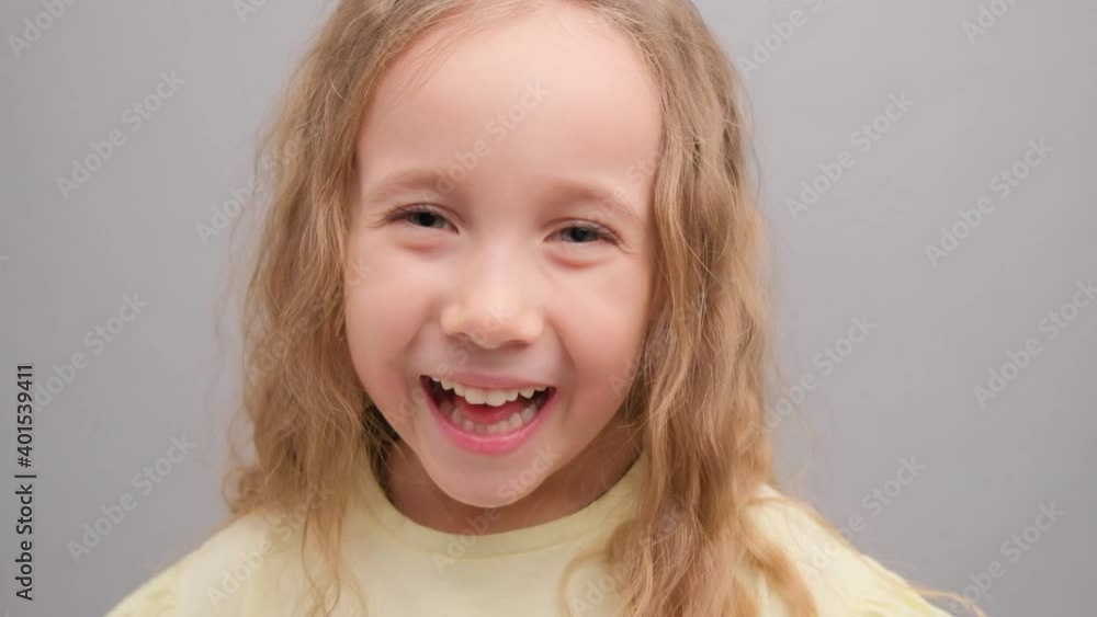 Little girl looks at the camera and laughs. Portrait of a child in the studio on a gray background close-up. Super slow motion. Little girl looks at the camera and laughs. Portrait of a child in the studio on a gray background close-up. Super slow motion.