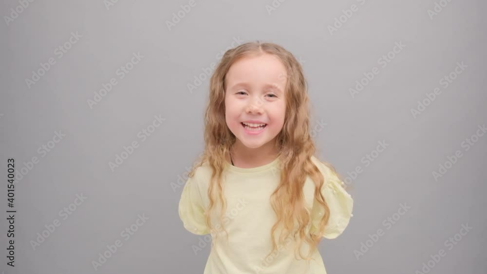 Little girl looks at the camera and laughs. Portrait of a child in the studio on a gray background close-up. Super slow motion. Little girl looks at the camera and laughs. Portrait of a child in the studio on a gray background close-up. Super slow motion.