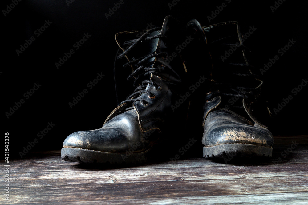 Old and torn black boots. Fashion shoes placed on black wooden floor