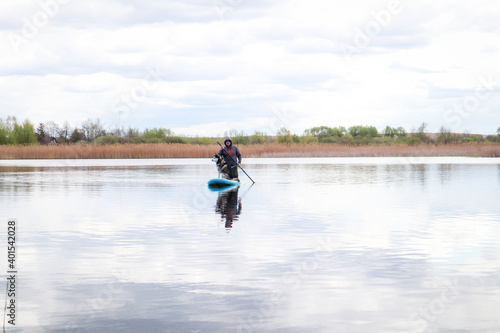 Man swims on a SAP board with a husky dog. Walk on the lake near the spring pine forest.