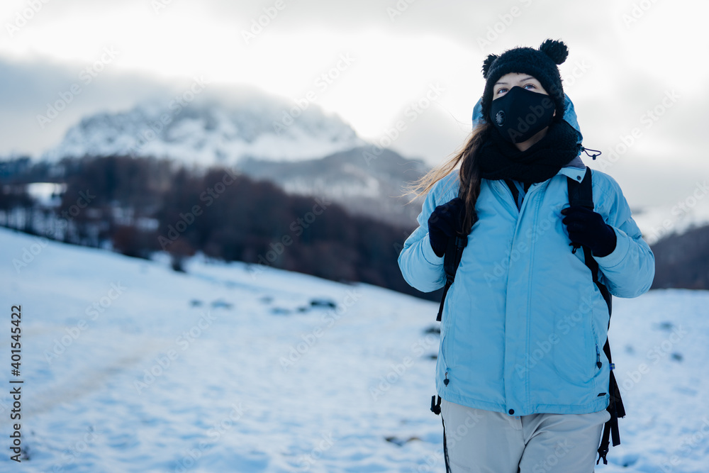 Female tourist wearing a protective mask in nature on mountain holiday vacation.Active vacation during the pandemic.Natural beauty.Hiker on a winter trek.Ski season,winter adventure.