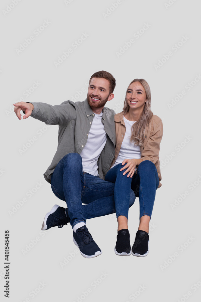 Fototapeta premium Couple Sitting on Floor Man Pointing to Side. Couple Isolated Watching Front. Relationship, Family, Lovers, Friends Concept