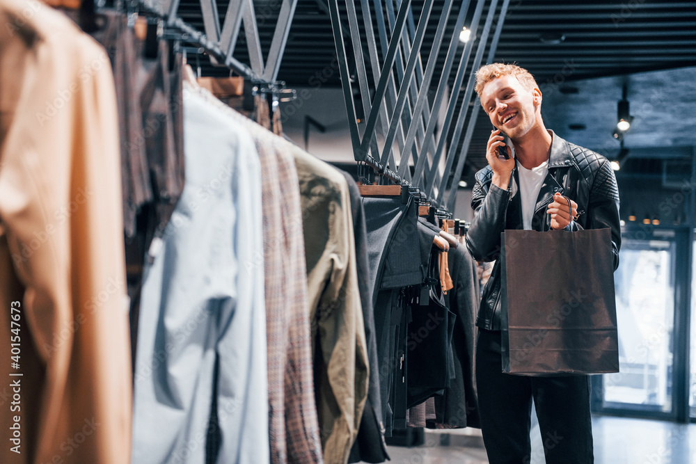 Talks by the phone. Young guy in modern store with new clothes. Elegant expensive wear for men
