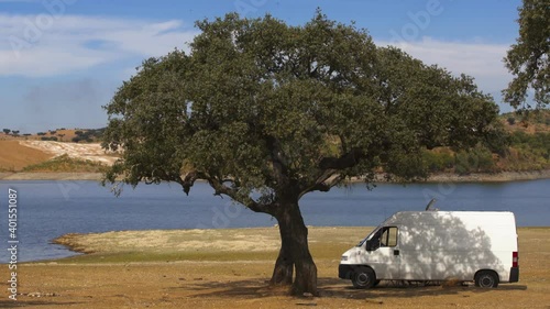 Camper van on an Alentejo dam landscape with the lake behind and under the shade of a tree, in Portugal photo