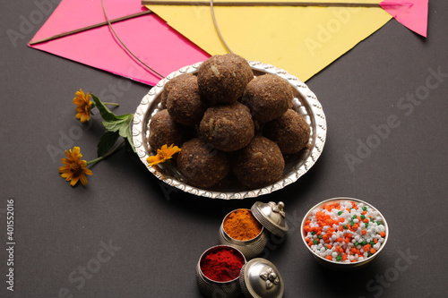 Til Gul OR Sweet Sesame Laddu with Kite model, haldi Kumkum and sugar crystals for Makar Sankranti festival over black background.