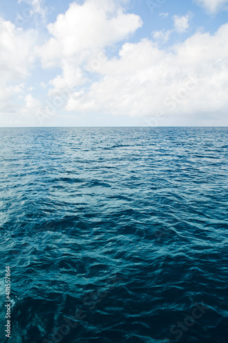 Deep ocean view with waves and white clouds. Relaxing seascape, endless sea, tropical waters background. Blue seas and skies separated by a far away horizon. Caribbean lifestyle themes