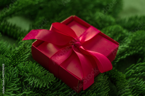 Pink gift box with a bow in the fir branches. Festive background with a gift. © Arylanna