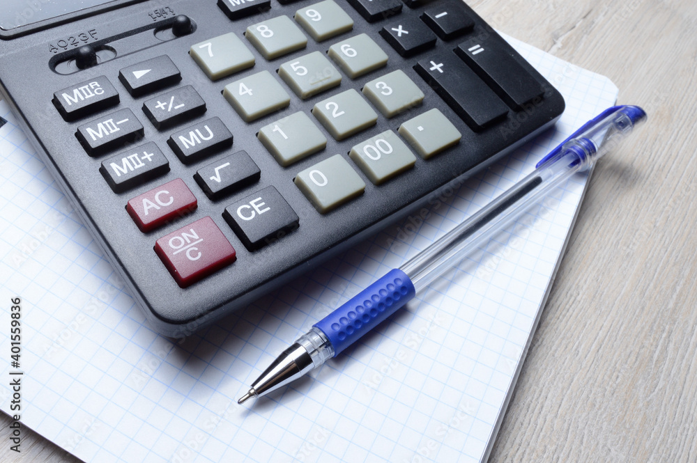 a ballpoint pen and a micro calculator lie on a squared notebook. close-up. a ballpoint pen and a micro calculator lie on a squared notebook. close-up.
