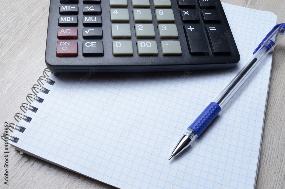 a ballpoint pen and a micro calculator lie on a squared notebook. close-up. a ballpoint pen and a micro calculator lie on a squared notebook. close-up.