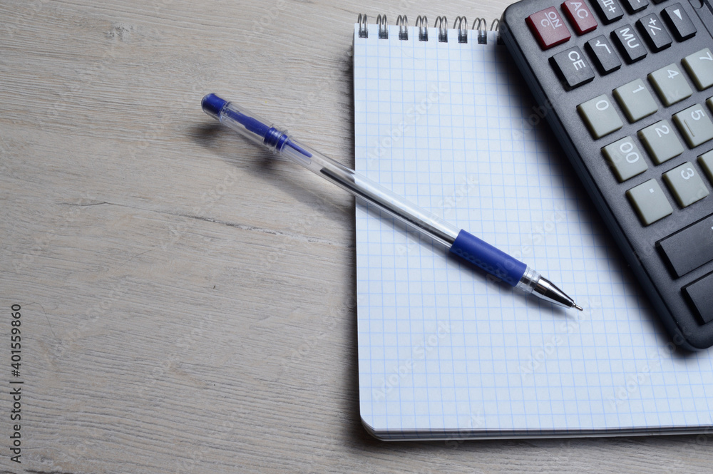 a ballpoint pen and a micro calculator lie on a squared notebook. close-up. a ballpoint pen and a micro calculator lie on a squared notebook. close-up.