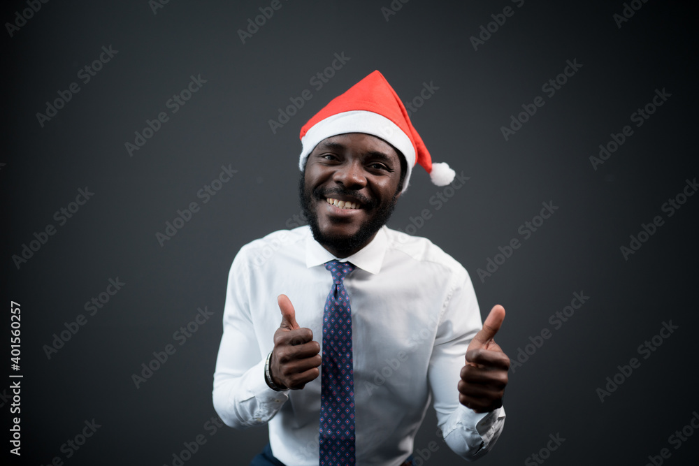 African american man in white shirt and tie with Santa hat on his head raises his thumb up and rejoices at christmas African american man in white shirt and tie with Santa hat on his head raises his thumb up and rejoices at christmas