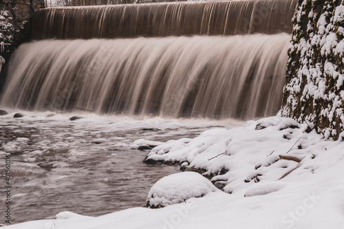 Two-storey waterfall in winter. Snowy rocks and river bank.