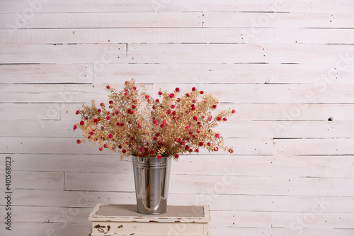House decoration concept: dried meadow flowers in a metal pot on a lighter background of wooden wall. Place for the inscription