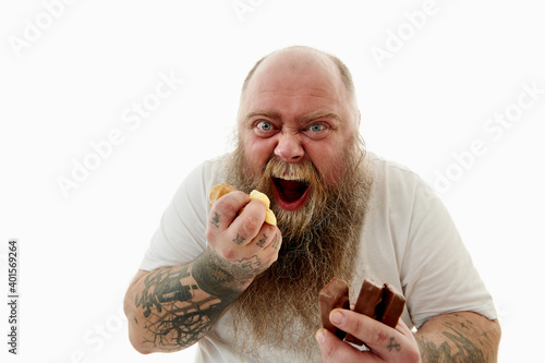 A man suffering from metabolic syndrome squeezes the cake into his fist and holds chocolate bars in his second hand. Сoncept of unhealthy nutrition and the harmfulness of simple carbohydrates photo