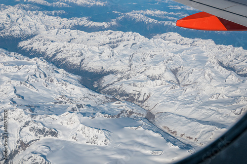 View of the snow-capped Alps and valley from an airliner porthole. Concept: air travel, aerial panoramas. Frame given by the airplane window