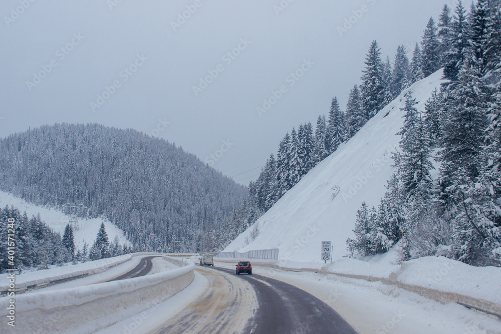 Snow-covered highway among the mountains, on the sides there are trees and trees in the snow. Winter landscape with snow-covered road, fir trees and mountains in Montana, America, 1-18-2020