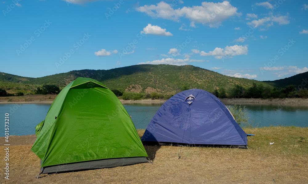 Multicolored tents on the shore of a mountain lake against the backdrop of inaccessible rocks surrounded by a green forest.