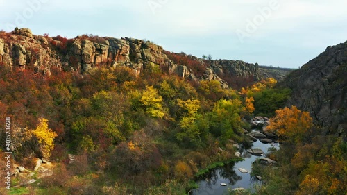 A stream flows in the Aktovsky Canyon, Ukraine. Autumn trees and large stone boulders around. Aerial UHD 4K drone realtime video, shot in 10bit HLG and colorized photo