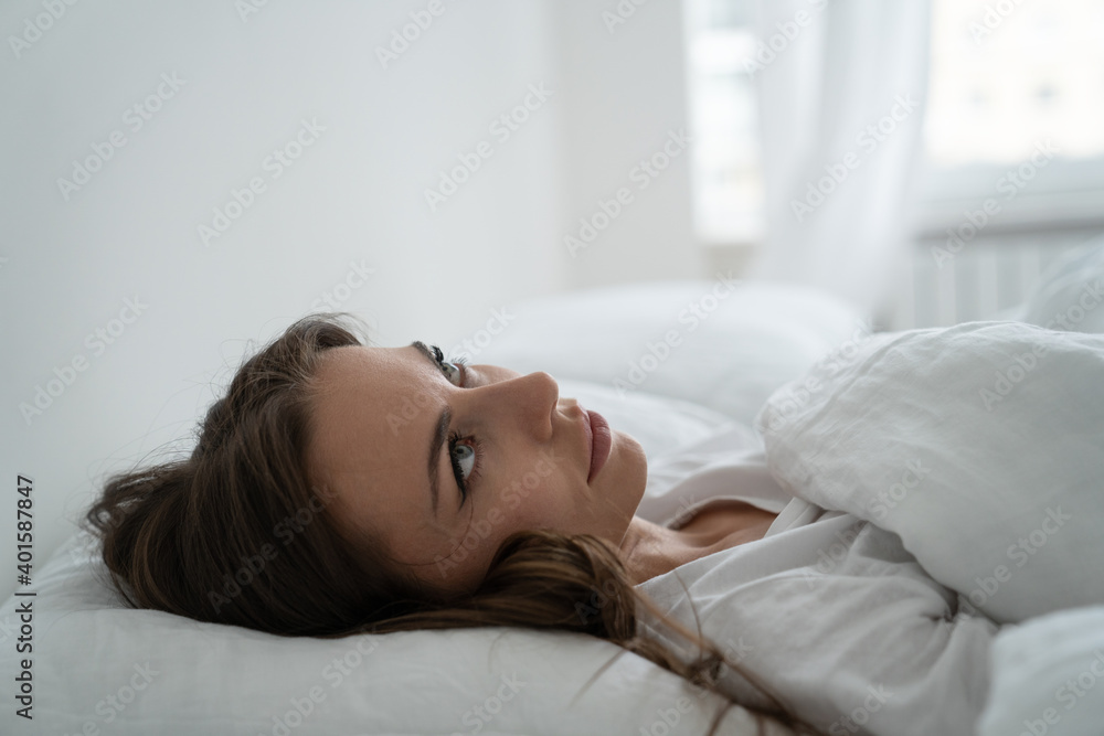 Angry woman annoyed by loud neighbors, looking up, suffering from insomnia or stress. Tired woman trying to falling asleep in bed at home in early morning. Sleep disturbance concept. Angry woman annoyed by loud neighbors, looking up, suffering from insomnia or stress. Tired woman trying to falling asleep in bed at home in early morning. Sleep disturbance concept.