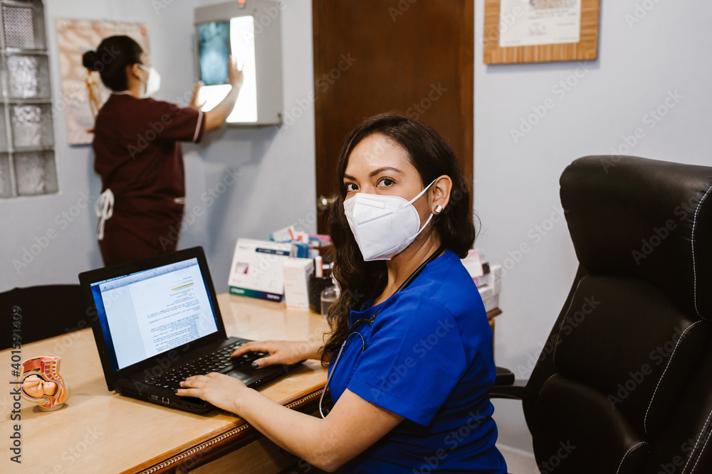 Latin female doctor working while sitting at desk in front of laptop in a Mexican hospital Latin female doctor working while sitting at desk in front of laptop in a Mexican hospital