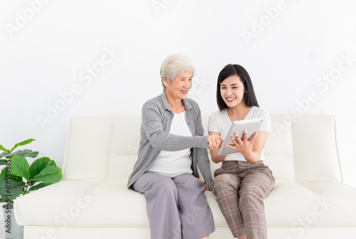 young Asian female and old female search information with tablet computer, they feeling happy and smile, they sitting on sofa, mother's day and happiness family time, technology and social network