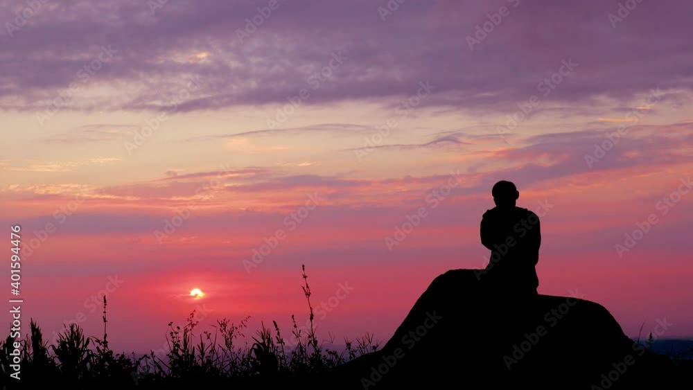 Man sitting in silhouette looking at the sunrise Man sitting in silhouette looking at the sunrise