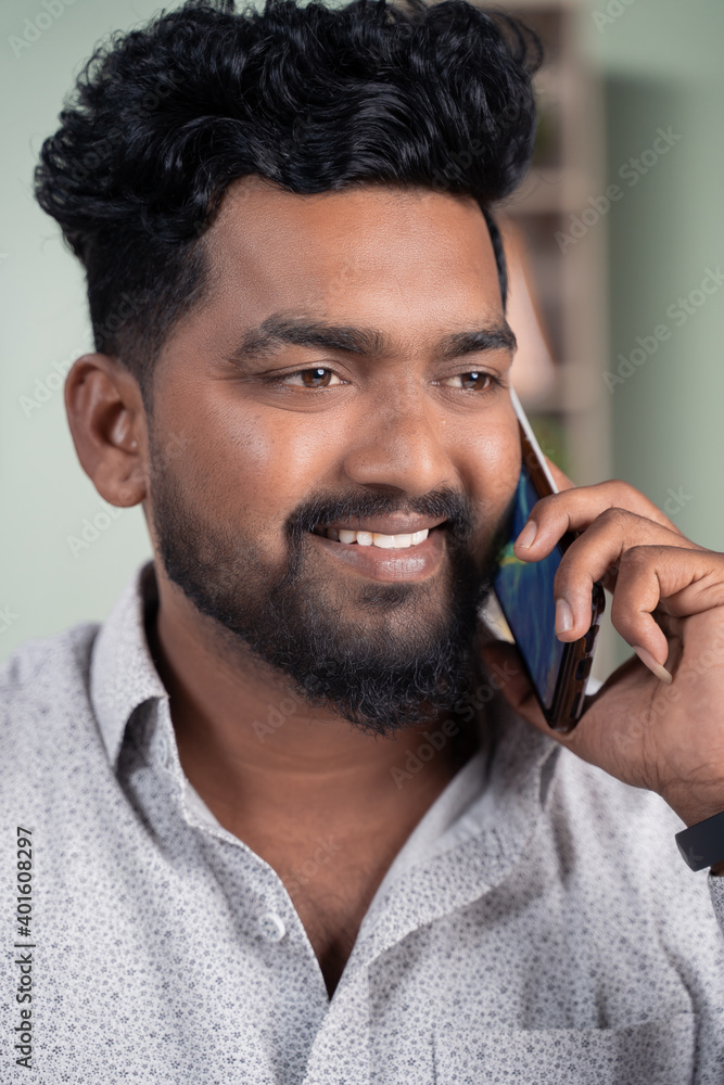 Close up of Smiling young Indian man busy talking or having conversation on mobile phone. Close up of Smiling young Indian man busy talking or having conversation on mobile phone.