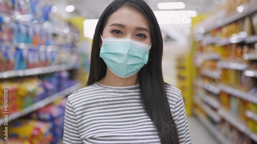 Young Asian woman in medical mask grocery walk toward camera shot, at supermarket during covid-19 coronavirus pandemic. Young lady stocks up food and toilet paper. © anon