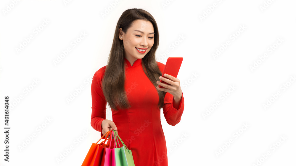 Asian woman wearing ao dai dress use smart phone and do the shopping with some bags on her hand Asian woman wearing ao dai dress use smart phone and do the shopping with some bags on her hand