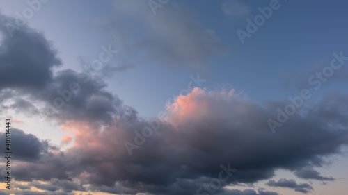 Evening sky, full screen. Lilac cumulus clouds with pink and gold backlighting against the blue sky