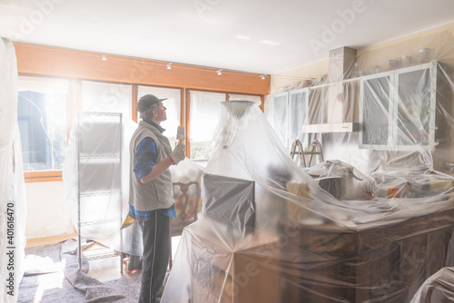 House painter painting the interior of a furnished house. Home renovation concept. Man is painting a kitchen protected with cover film