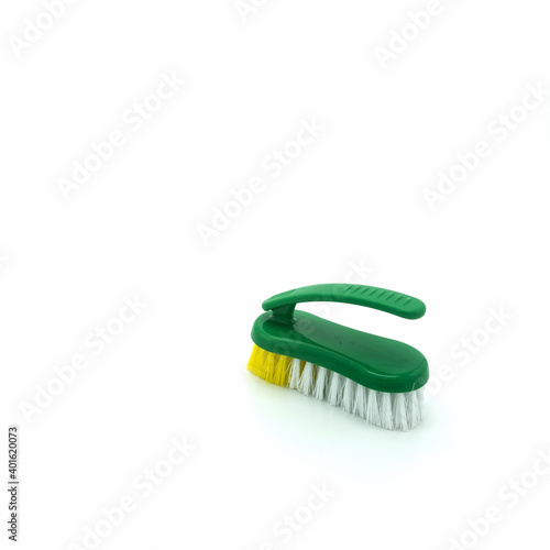 Plastic brush for cleaning the house. Green base  ribbed  non-slip handle. The bristles are thick and long  white and yellow. Isolated on white background. Bottom right corner.