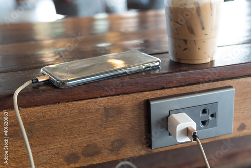 Smart phone while charging battery on wood table.
