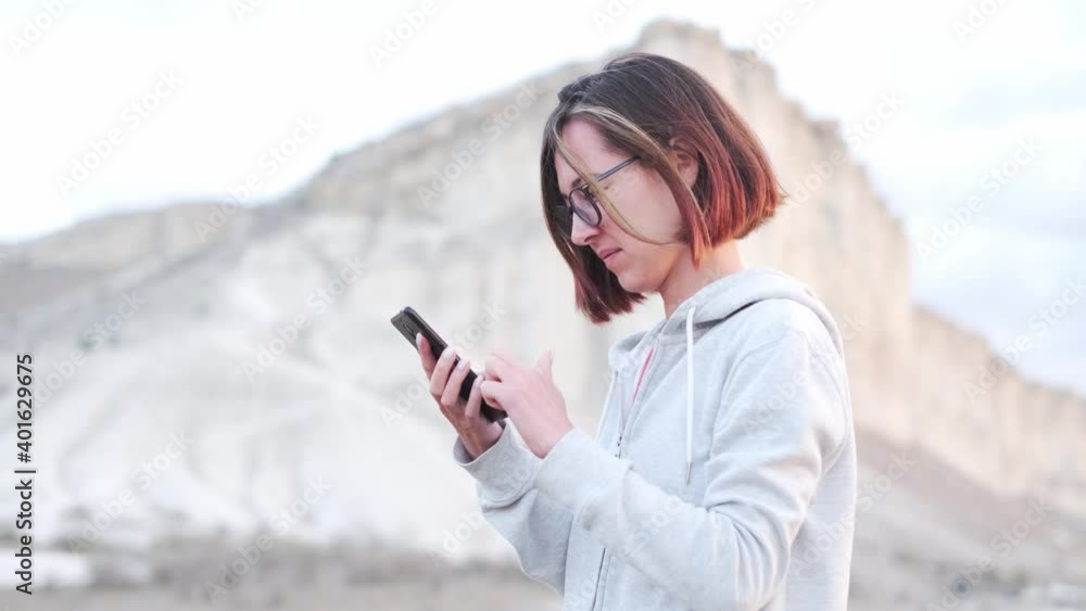 Traveler young woman using smartphone on background of Ak-Kaya white rock, Crimea. Traveler young woman using smartphone on background of Ak-Kaya white rock, Crimea.