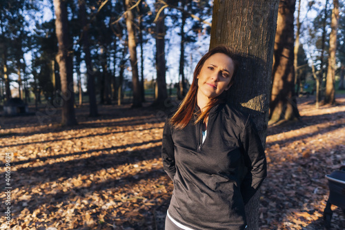 pensive and happy beautiful woman leaning on a tree in the forest at sunset after taking a walk. exterior concept, enjoy