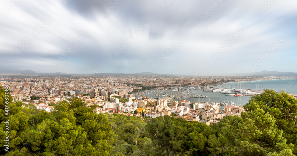 Panoramic view of the city of Palma de Mallorca with a forest in the foreground and clouds in motion