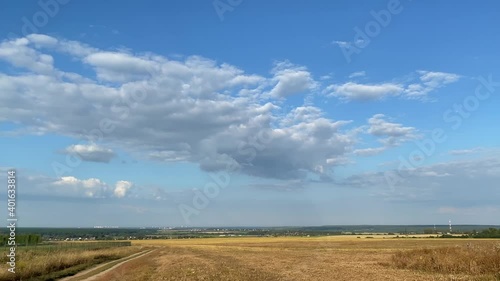 A field of harvested wheat is illuminated by the bright summer sun. White clouds float in the blue sky.