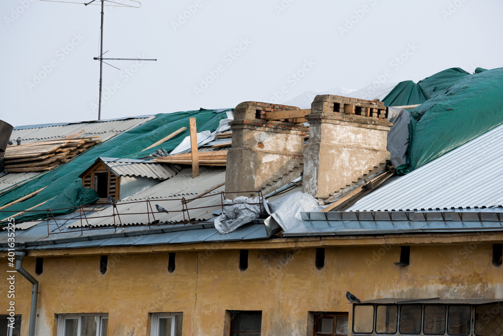 Roof repairs of an apartment building. The roof collapsed under the weight of snow. Damaged falling roof and chimney on sunny day with clear blue sky.