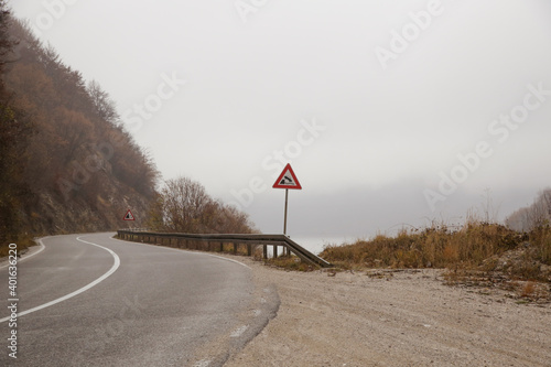 Curvy road in mountain area with falling off a cliff warning traffic sign. photo