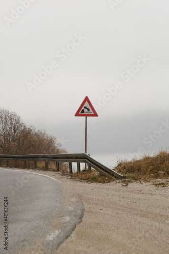 Curvy road in mountain area with falling off a cliff warning traffic sign. photo